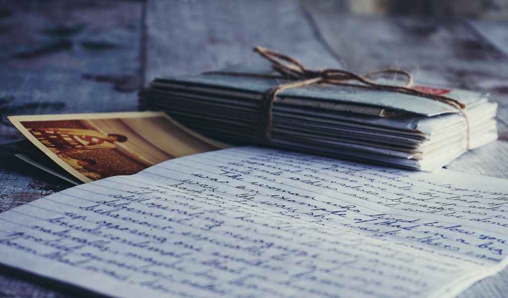 Handwritten letter laying on wood table with a photograph tucked underneath the letter and a stack of envelopes tied together with a piece of brown string off to the side.