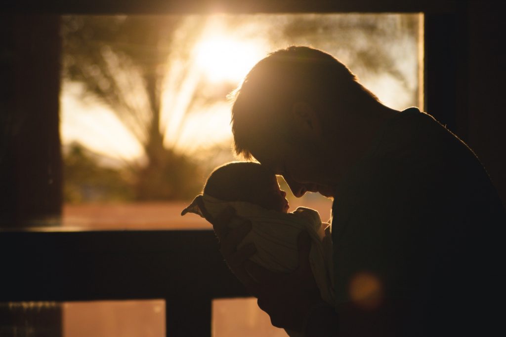 Profile of a father holding newborn wrapped in blanket with sun light in the background