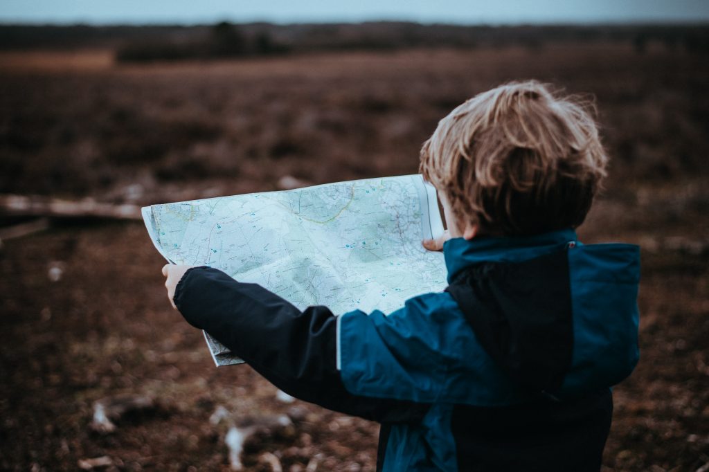 Small child looking at map wearing a blue and black jacket facing towards the horizon.