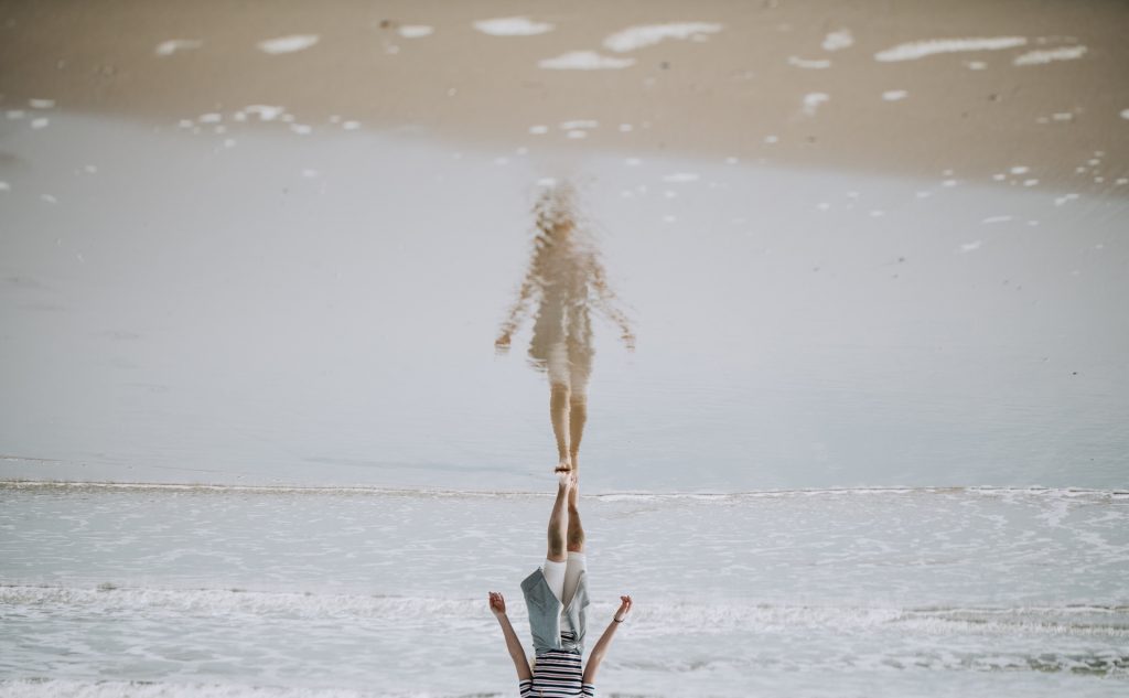 girl on beach with reflection of self on shallow water