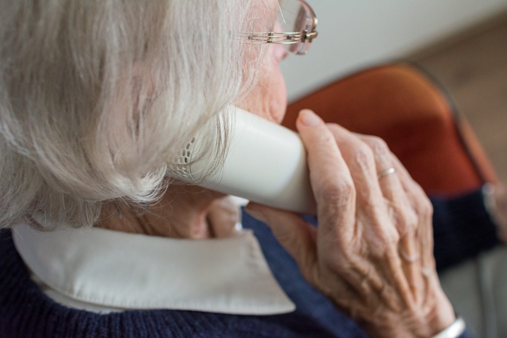 An elderly lady with glasses sitting in a chair talking on the telephone.