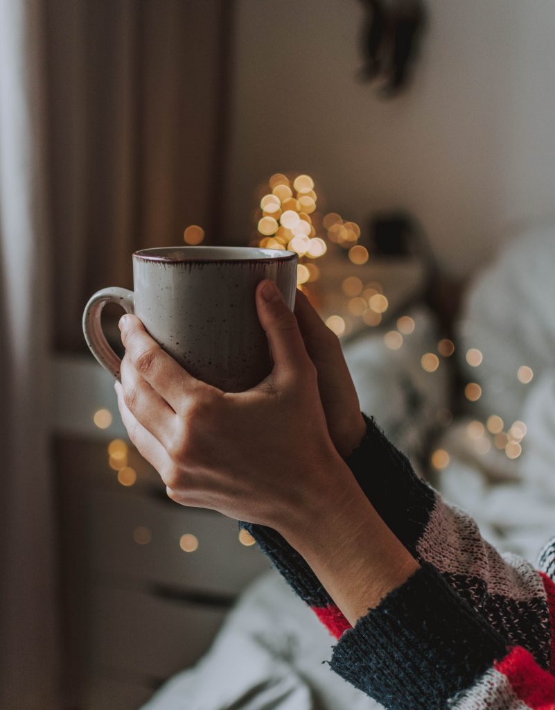 person holding gray mug with gold light in background