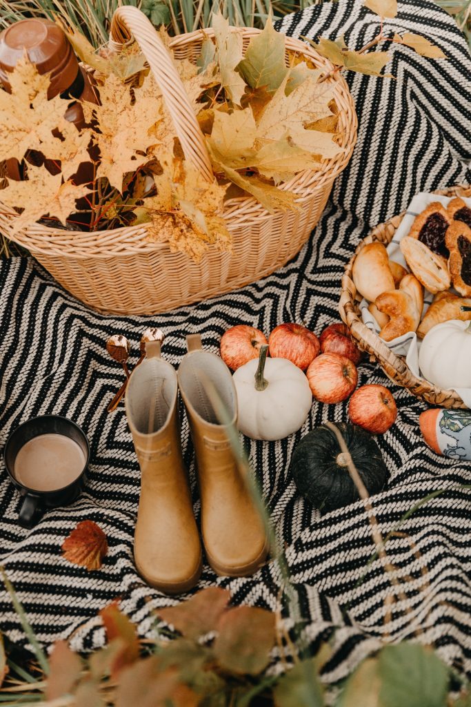 Fall collection with basket of leaves, tan colored boots, orange pumpkins and tray of pastries