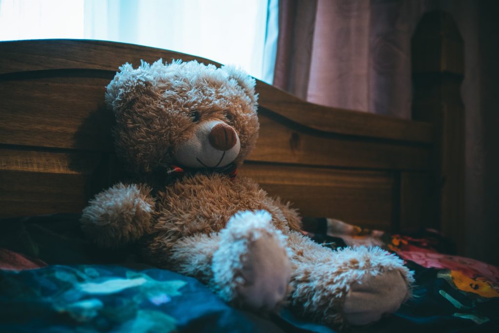 Brown teddy bear leaning up against headboard of bed