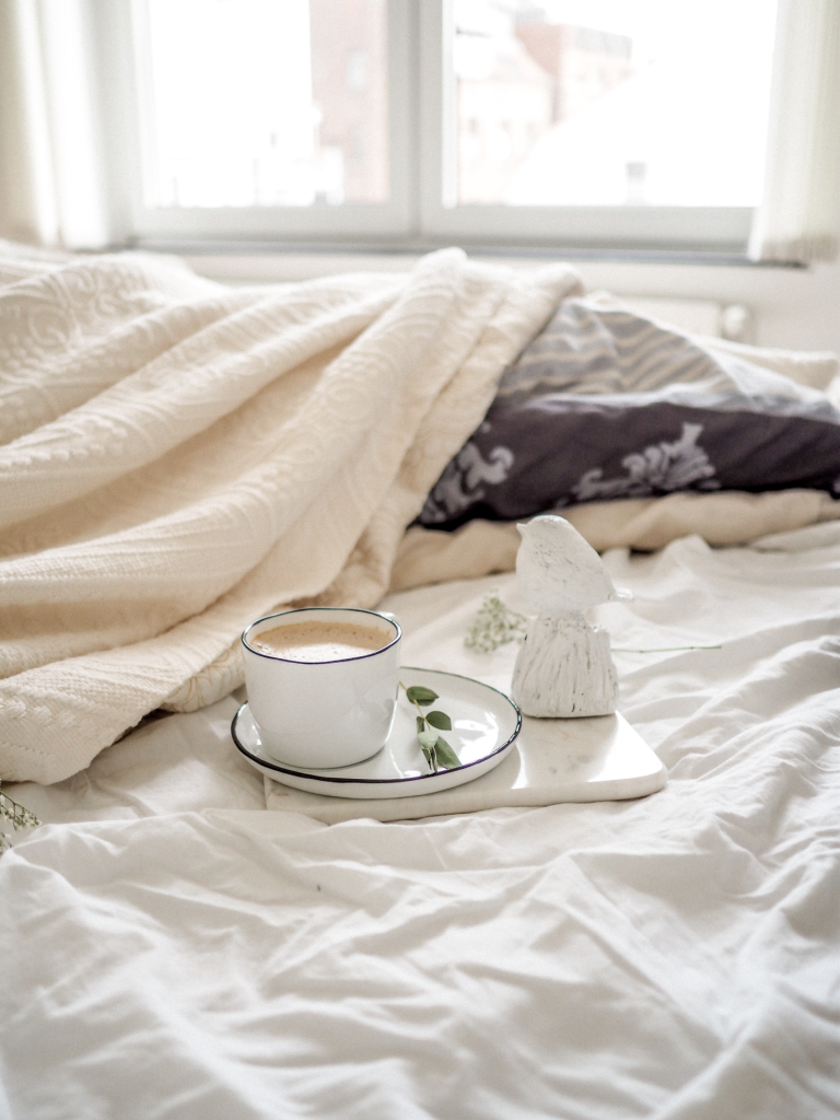 Bed with white and cream colored blankets with cup and saucer