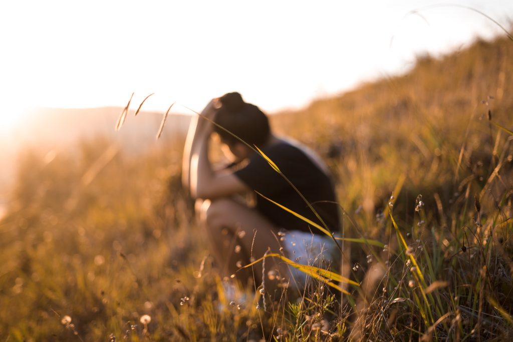 Woman sitting on grassy hillside with blurred sunlight in distance