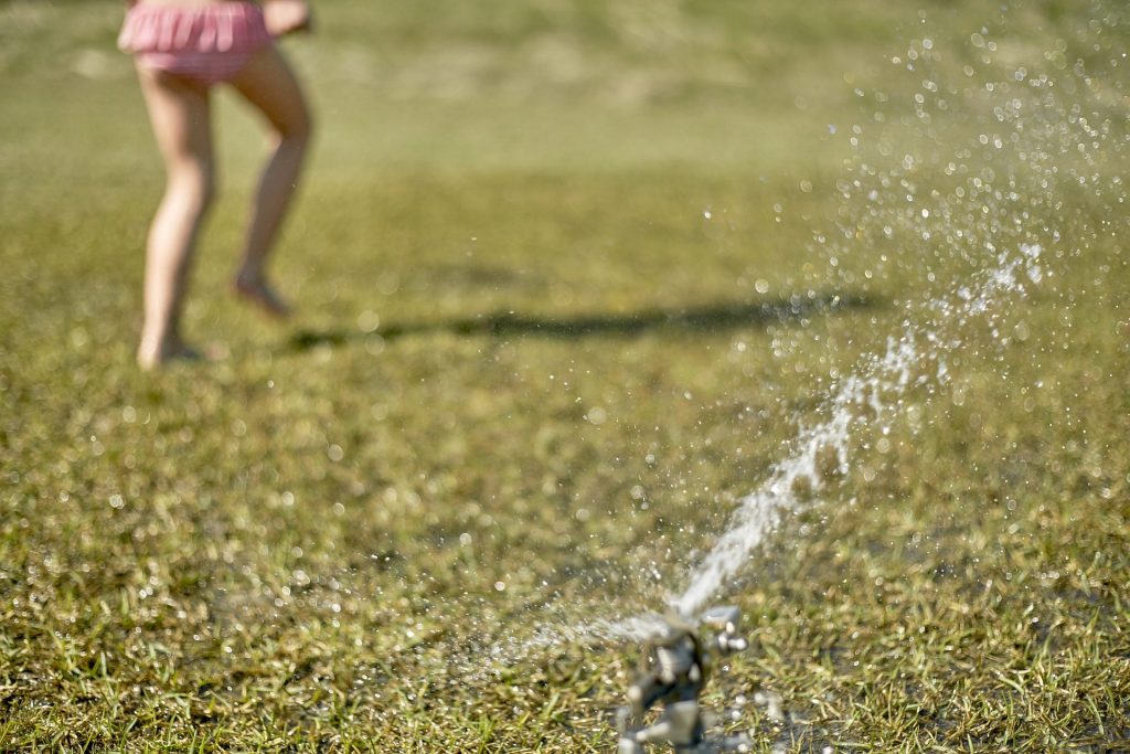 Small child in pink bathing suit playing in sprinkler