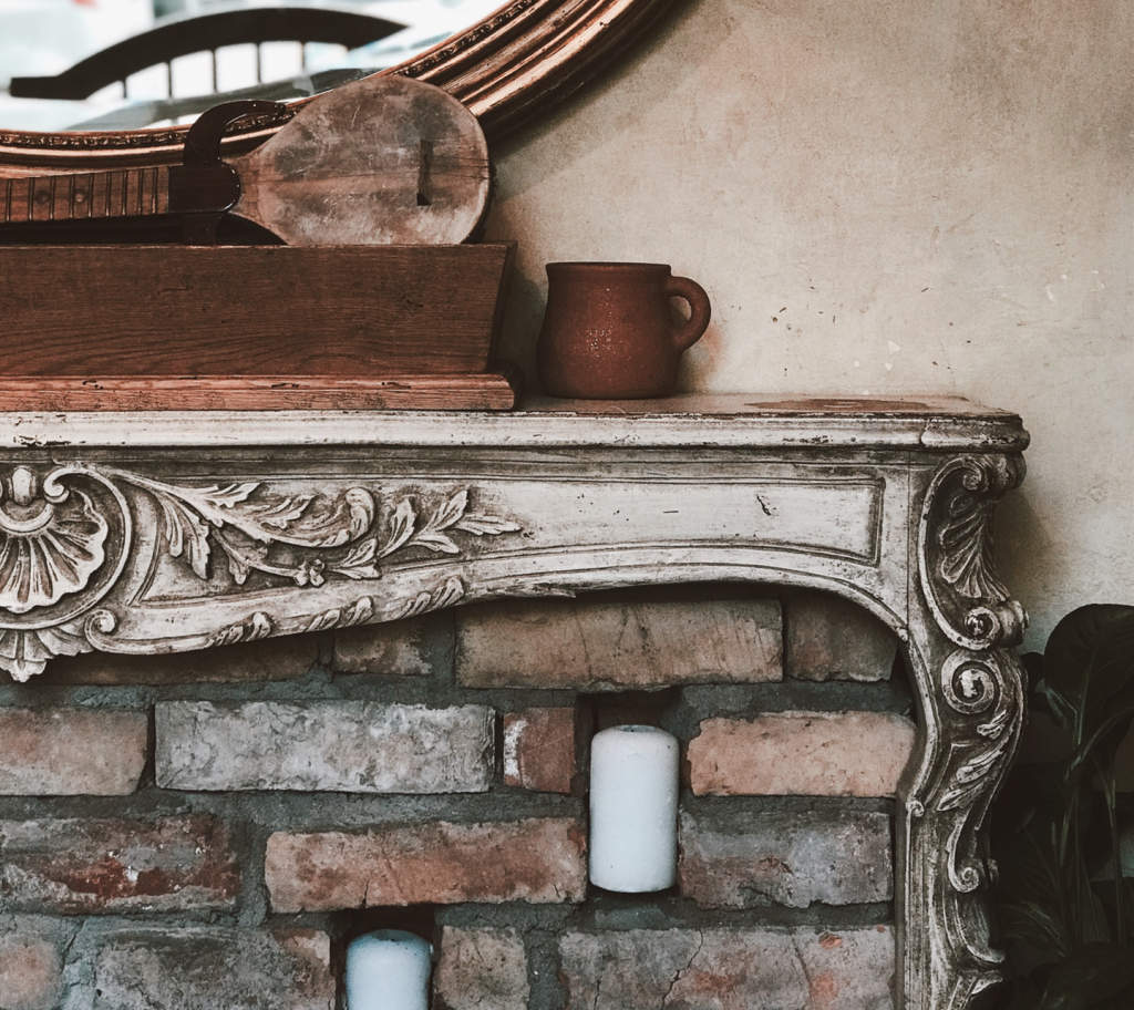 Brick fireplace and ornate wood mantle with mug and wood box with mirror in background