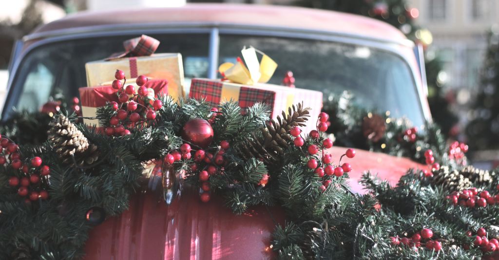 Back end of old red car with Christmas packages and green garland and red berries on top