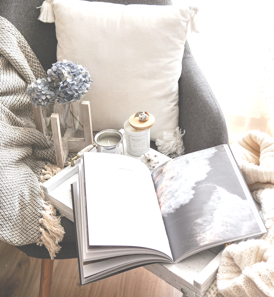 Chair with white pillow and blanket with side table with book and blue flower