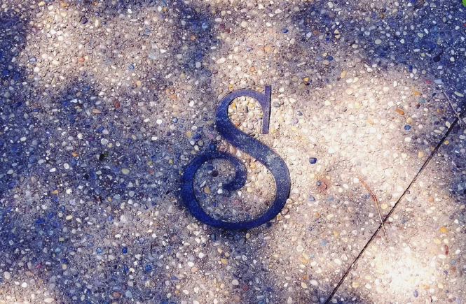 Close up image of "S" on a sidewalk with a pair of feet in tennis shoes