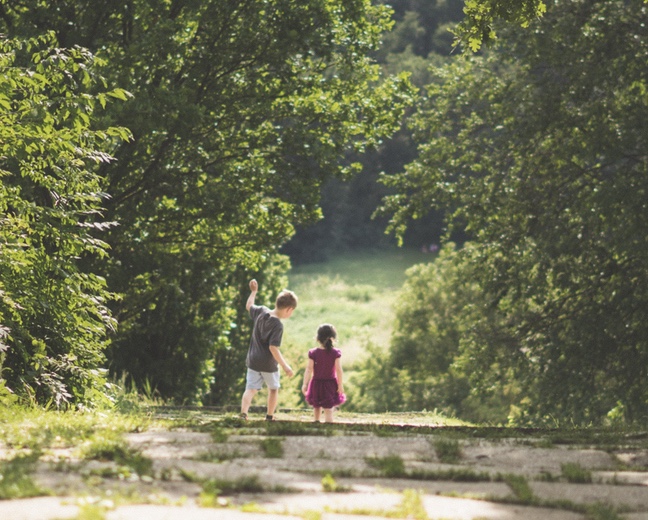 Little boy and girl walking down a road into the green trees