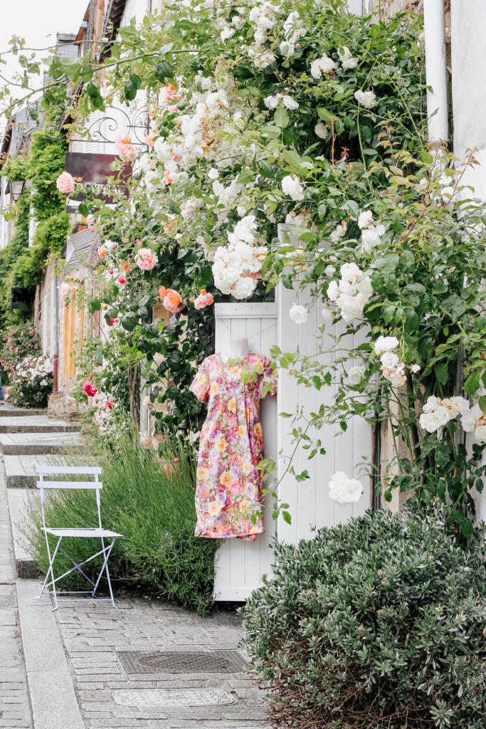 Side view of multiple boutiques with climbing roses, patio chair, and floral pink/orange summer dress hanging up