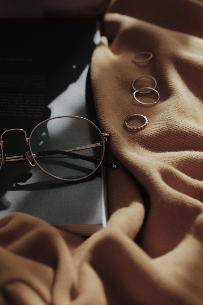 Close up image of reading glasses, gold rings on top of light tan blanket.