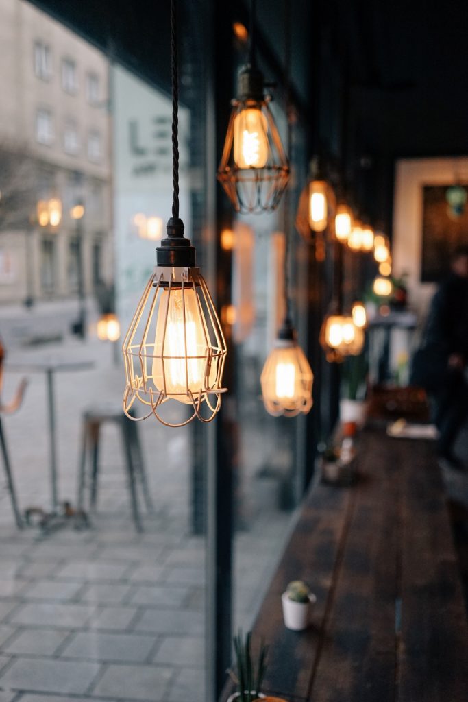 Multiple gold hanging lights inside a cafe set up against a window facing outside