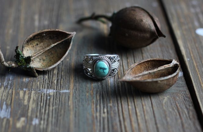 Turquoise stone, silver ring with nuts on top of wood table