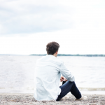 Young male adult sitting on beach looking at ocean