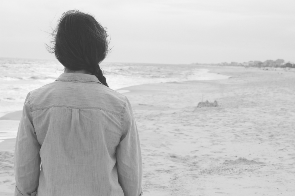 Black and white photo of girl standing on beach looking at ocean