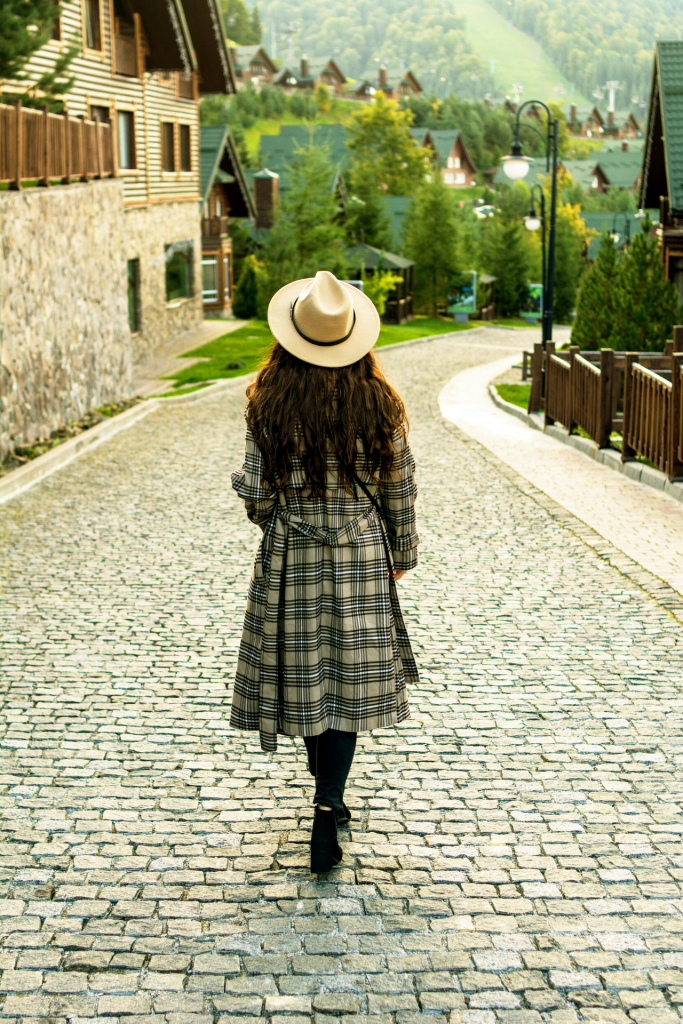 Girl with plaid coat and hat walking down cobblestone street