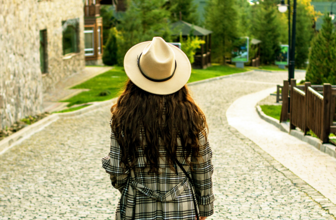 Girl wearing hat and plaid coat walking down cobblestone street