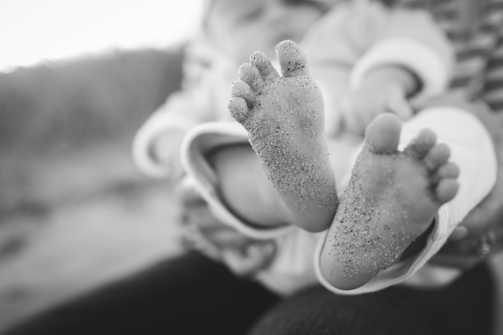 Black and white image of baby with feet covered with beach sand