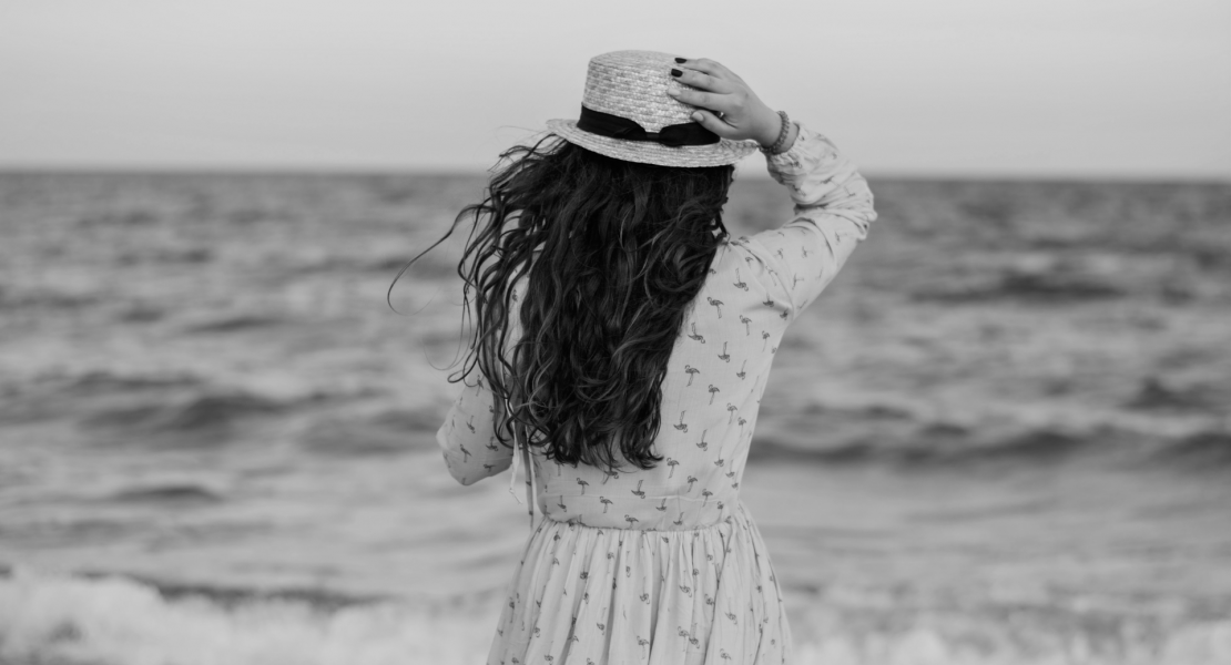 Black and white image of girl with hat looking out at sea
