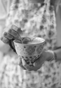 Black and white image of lady holding teacup stirring with spoon