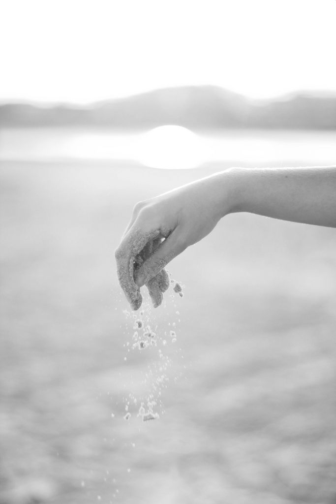 Black and white image of lady's hand dropping grains of sand